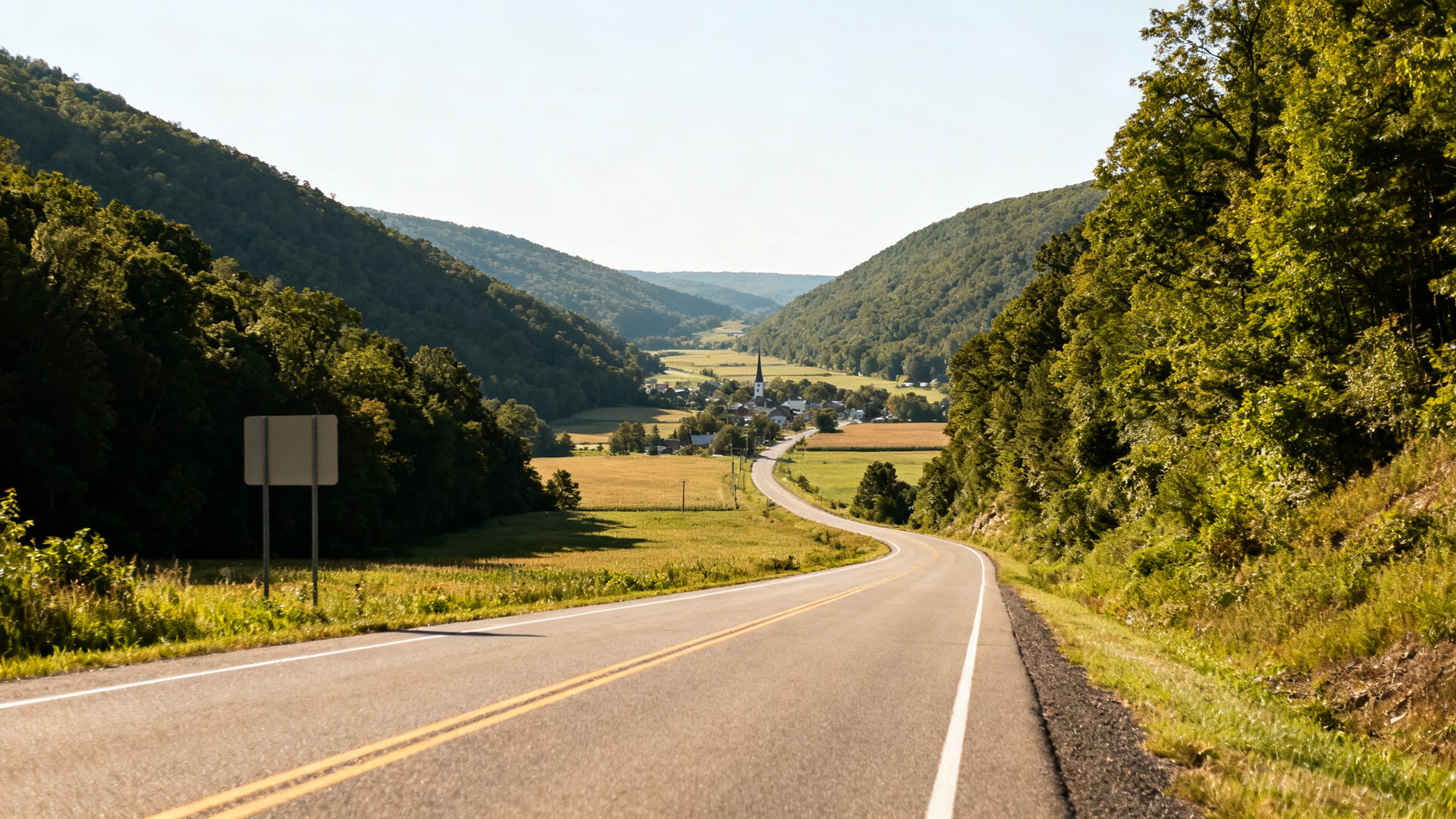 A two lane road through a green central Pennsylvania valley with a small town in the distance